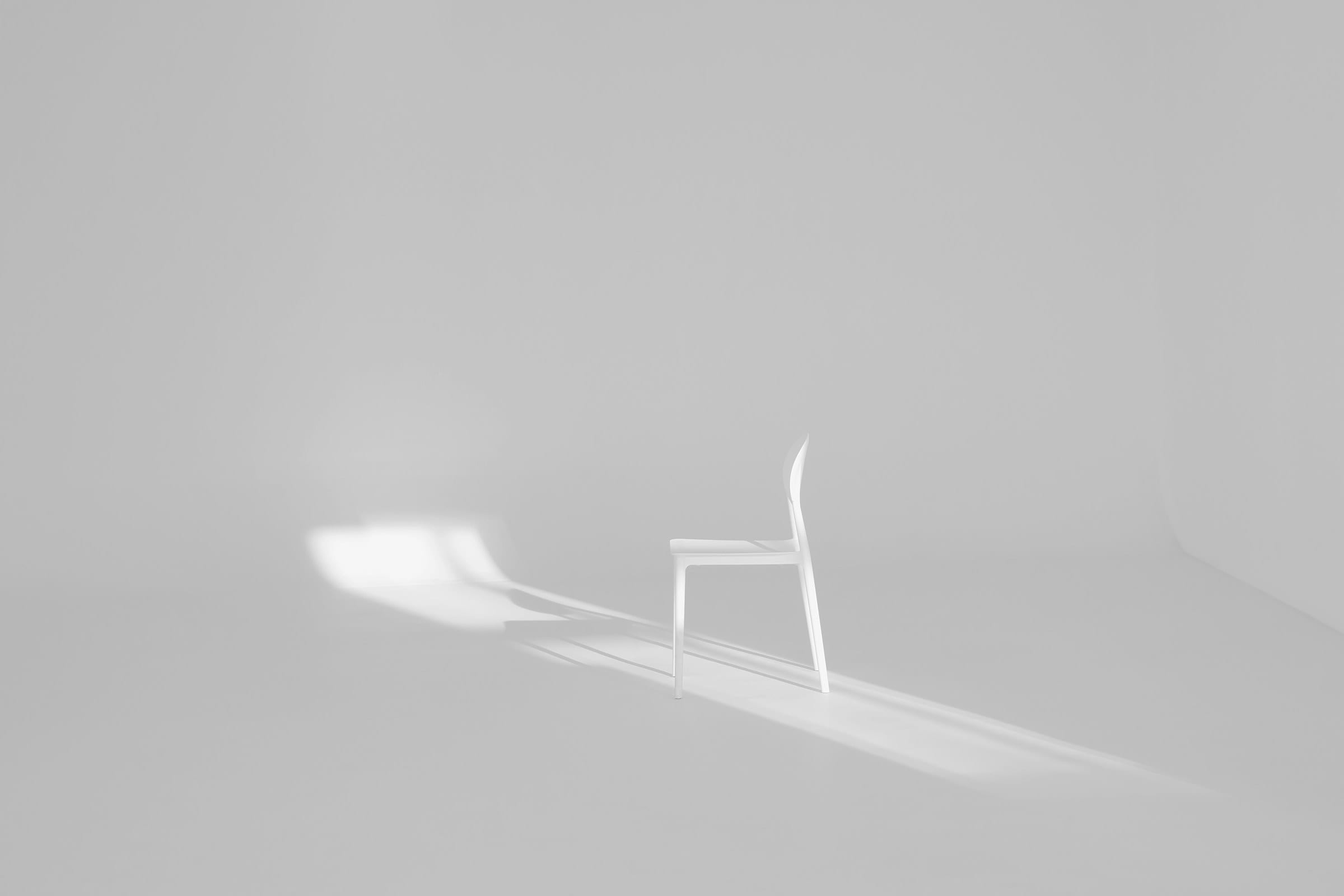 A single white chair and its shadow in a bright, empty room
