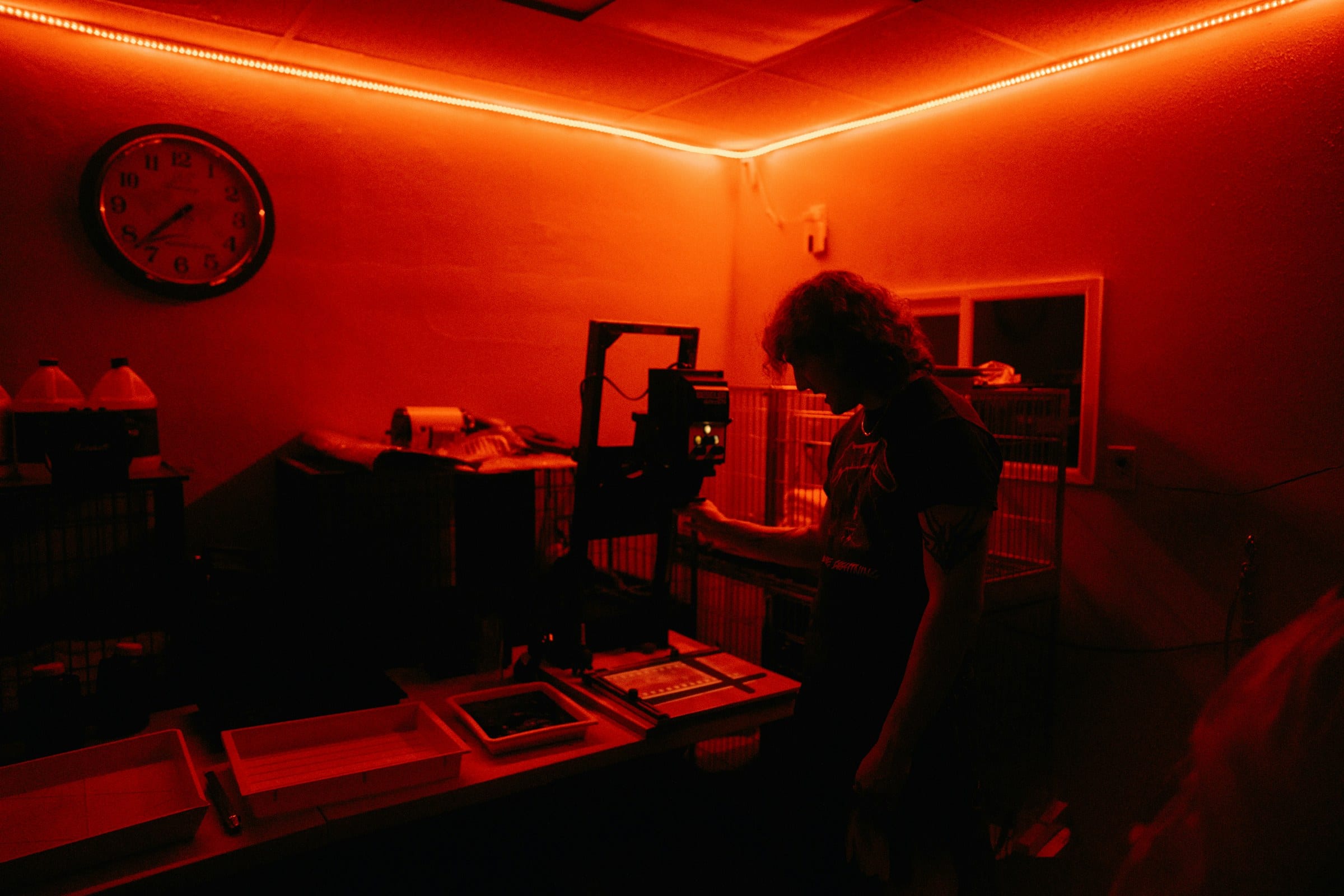 A darkroom lit red by safelights, with an enlarger on the bench