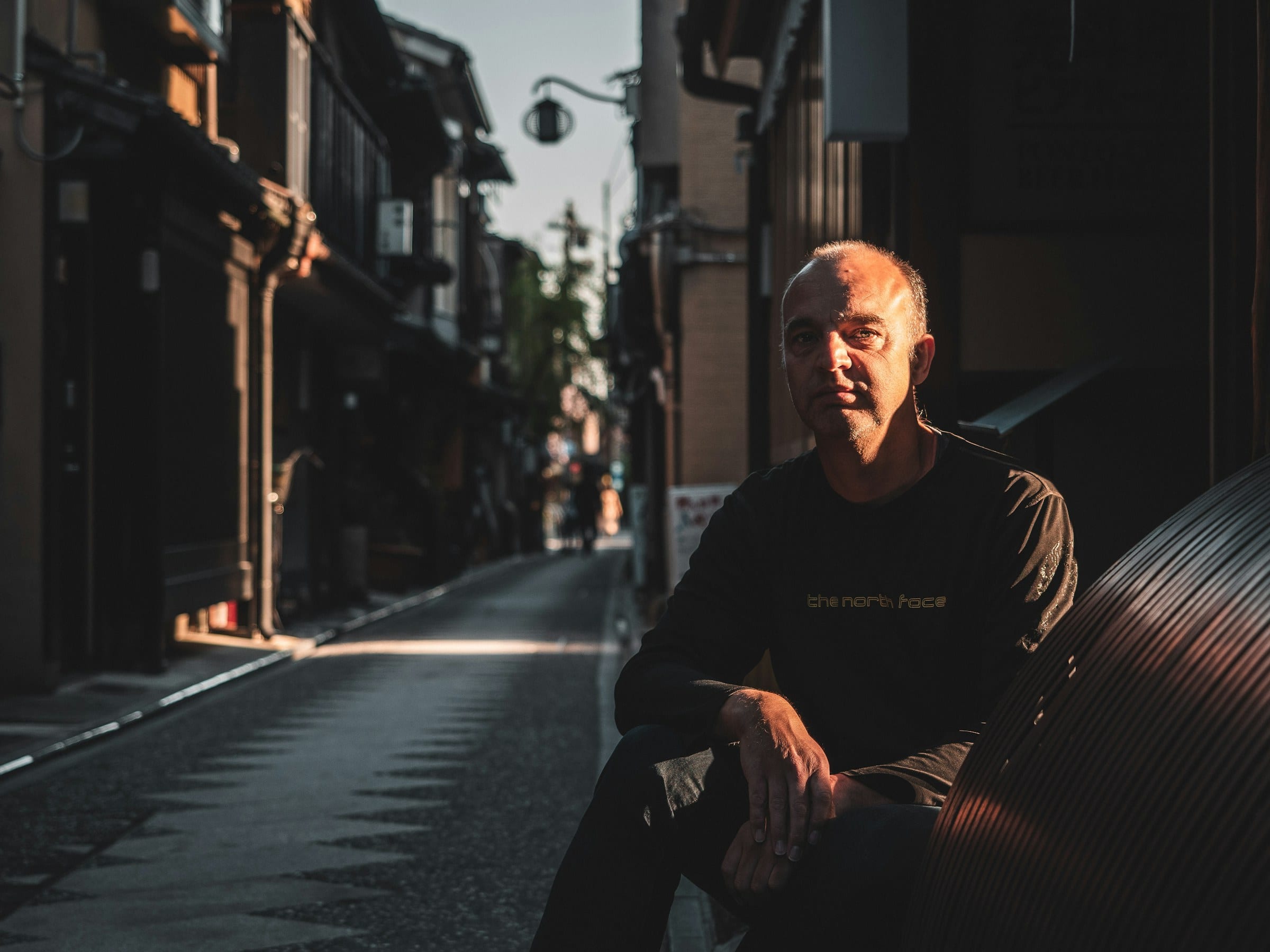 A man seated in a quiet Kyoto alley in late light