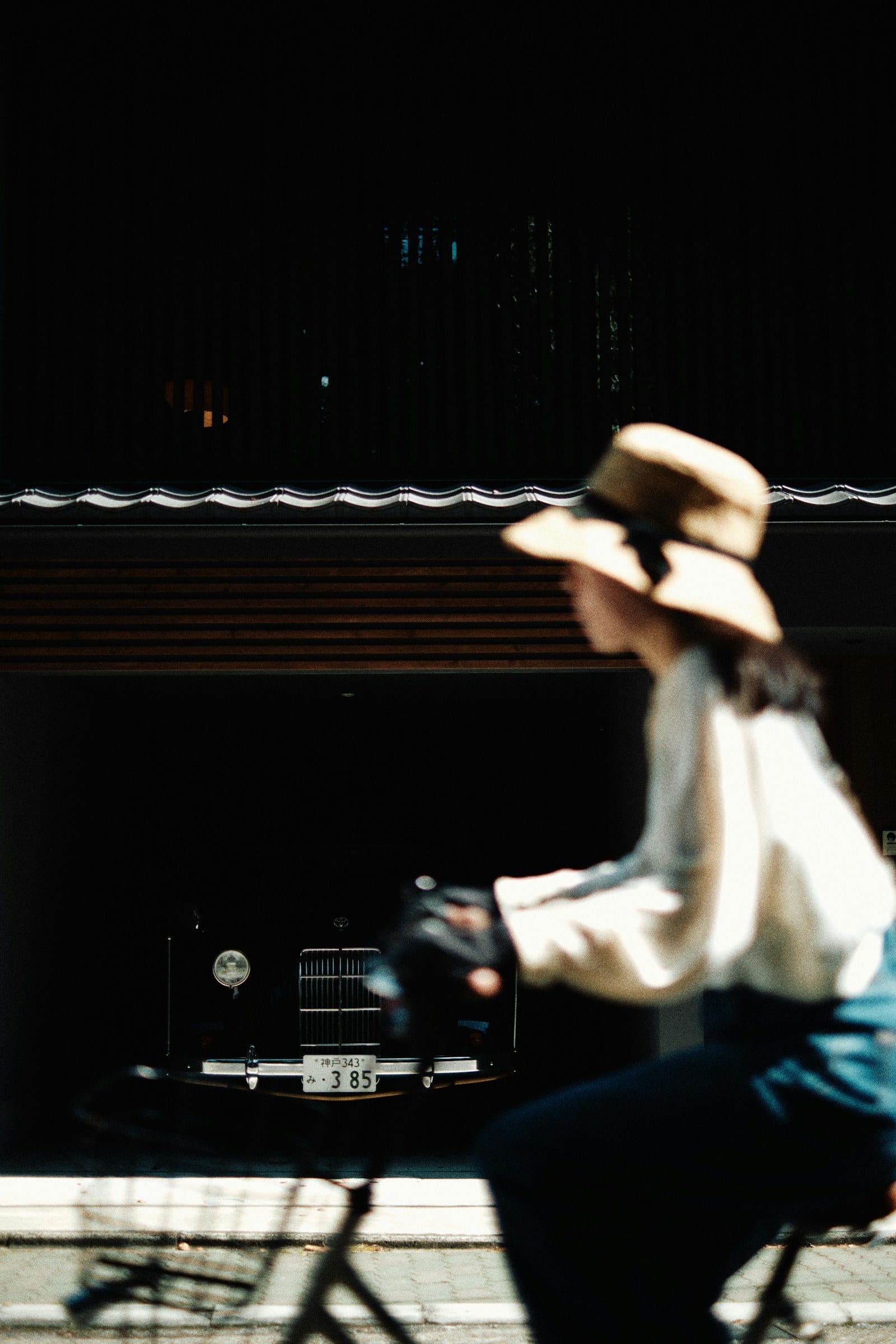 A cyclist in a wide-brimmed hat passing through a dark Kyoto street