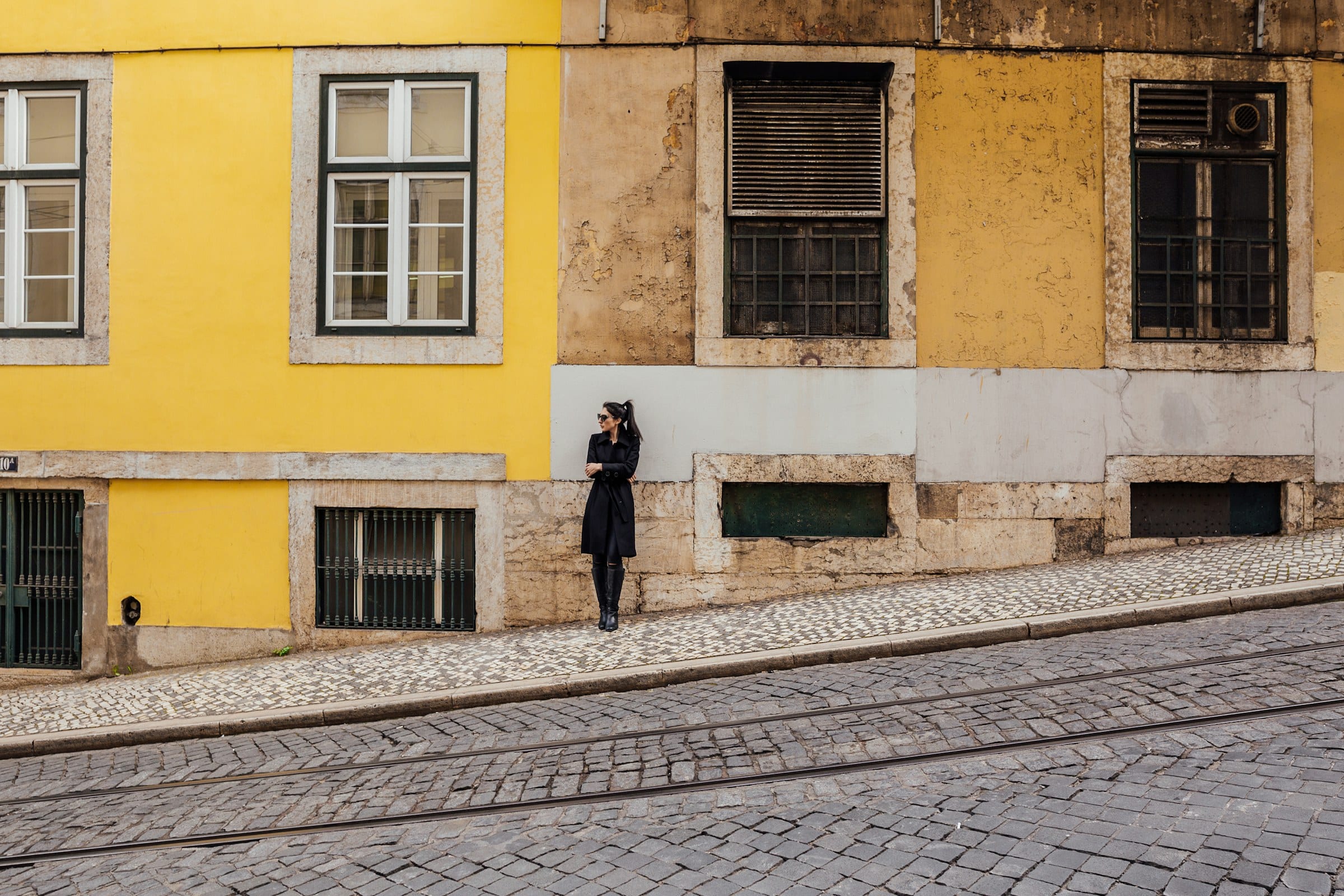 A lone figure against a yellow tiled façade on a Lisbon street