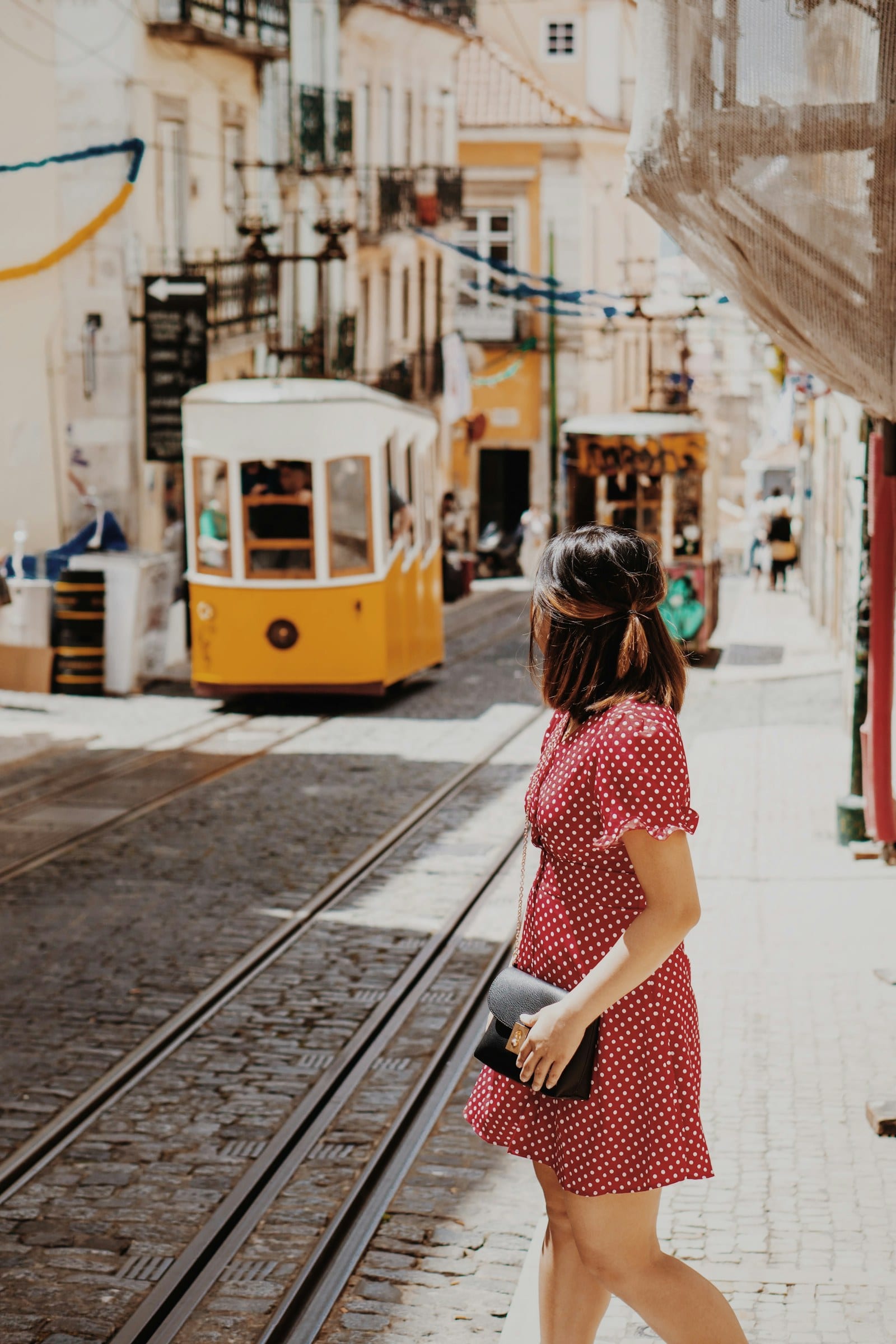 A woman in a red dress crossing tram tracks beside a yellow Lisbon tram