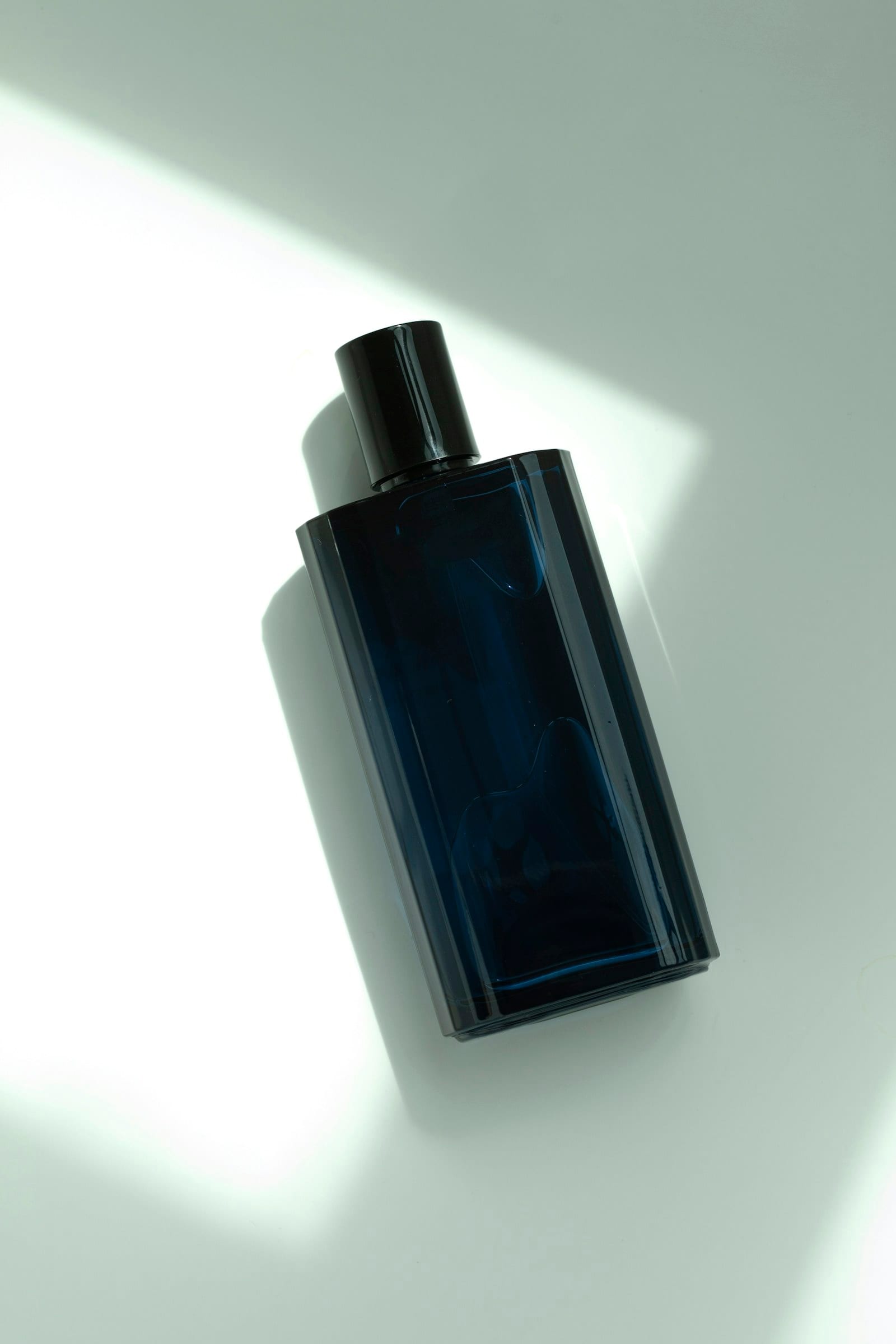A dark blue glass bottle lying in a shaft of sunlight on a pale surface