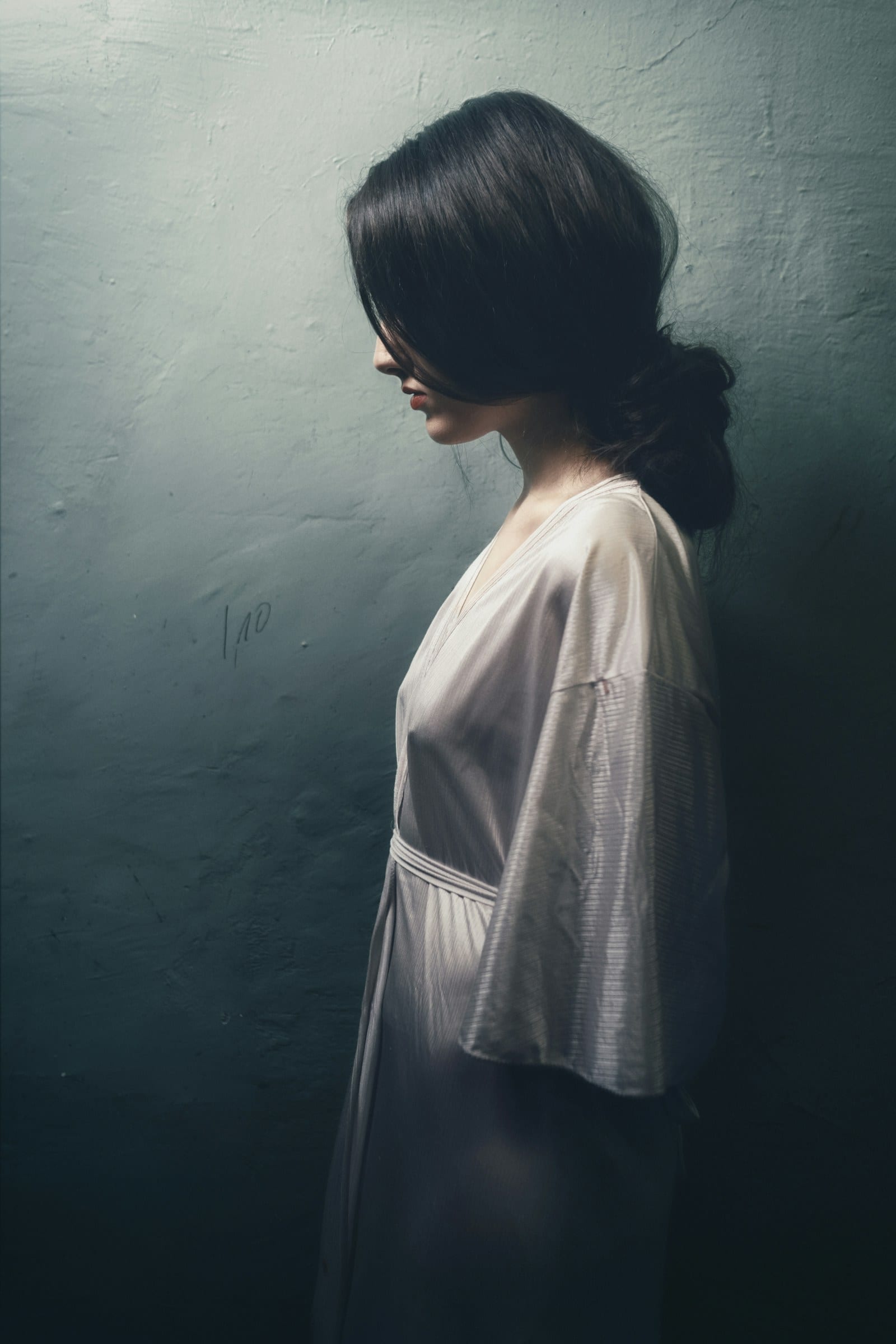 A woman in a white dress in profile against a dark blue wall