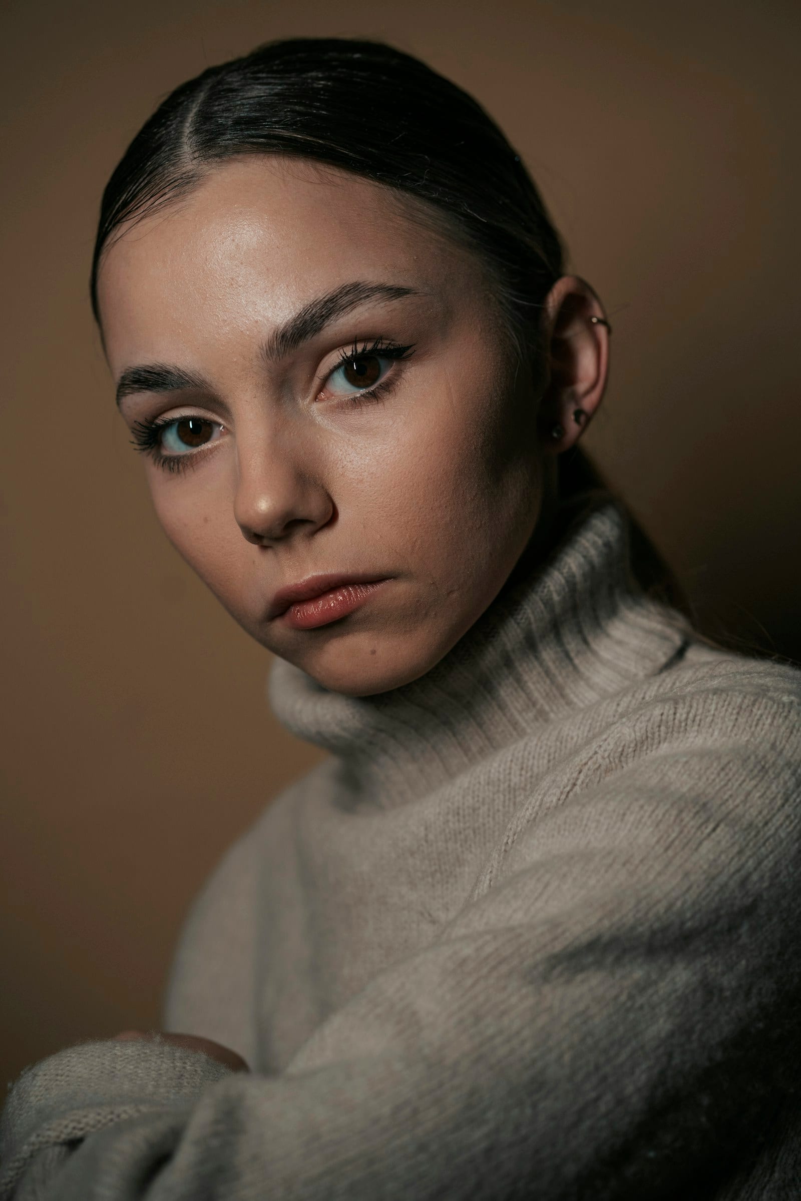 A portrait of a woman in a cream knit against a warm dark background